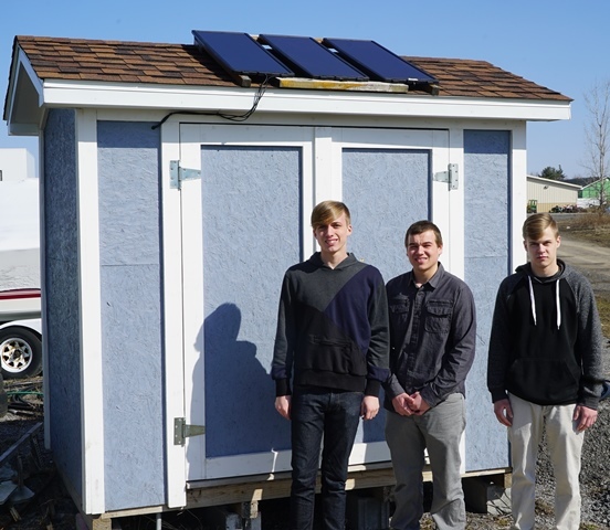 Students Sean Spezzano, Dylan Hartle and Bryan Nielsen stand in front of shed with solar panels