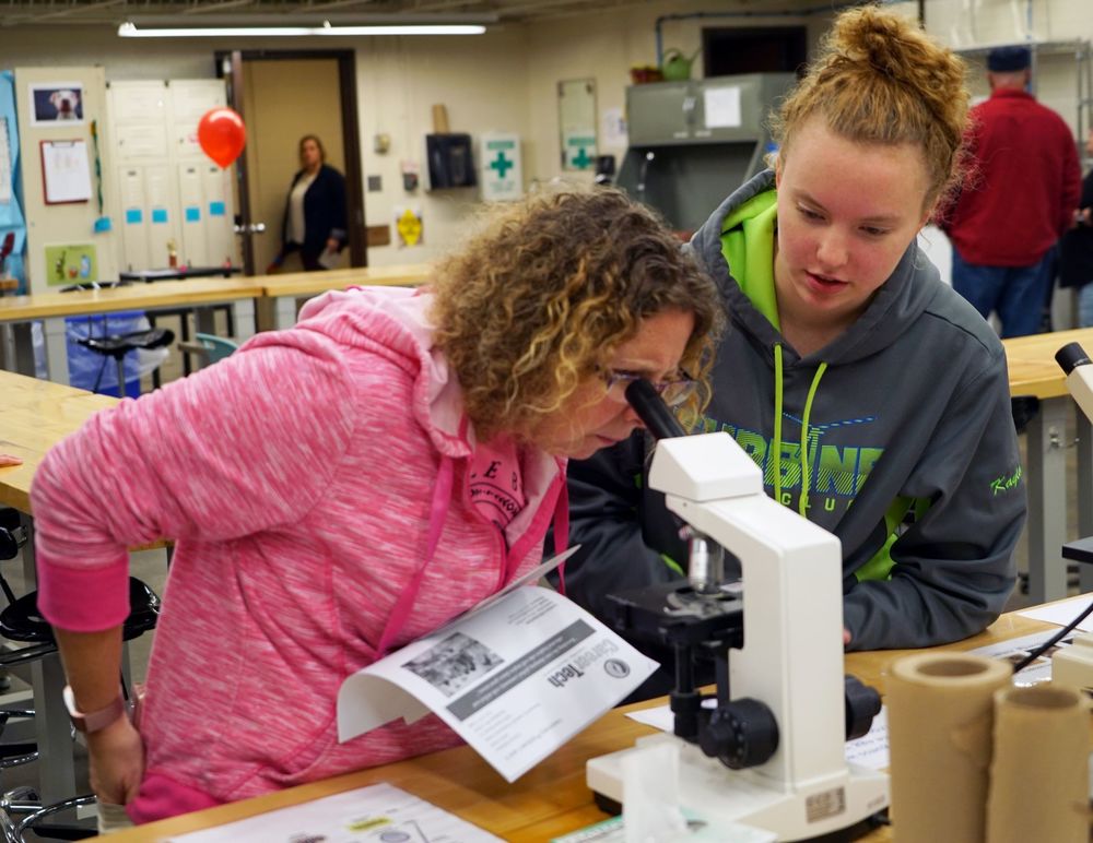 parent looking into microscope next to student 